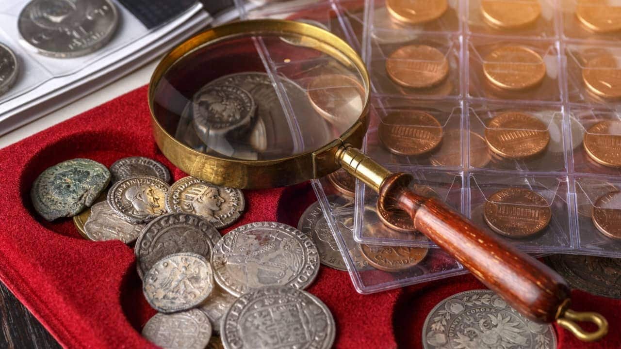 Várias moedas antigas sob lupa, em um superfície vermelha