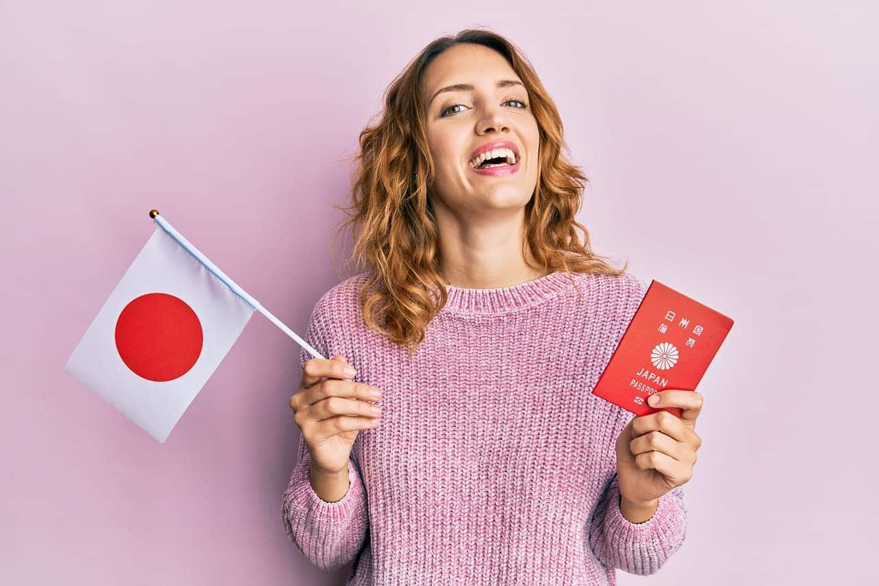 Jovem mulher caucasiana segurando a bandeira do japão e passaporte sorrindo