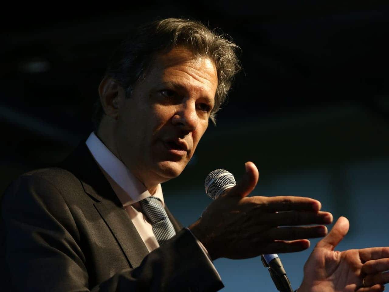 foto de Fernando Haddad, falando ao microfone, vestindo de terno e gravata