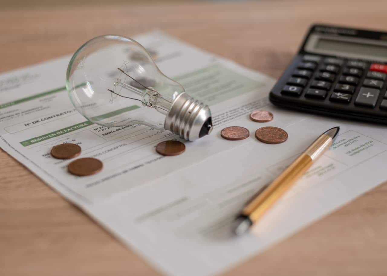 Moedas, lâmpada, calculadora e caneta em cima de uma conta de luz