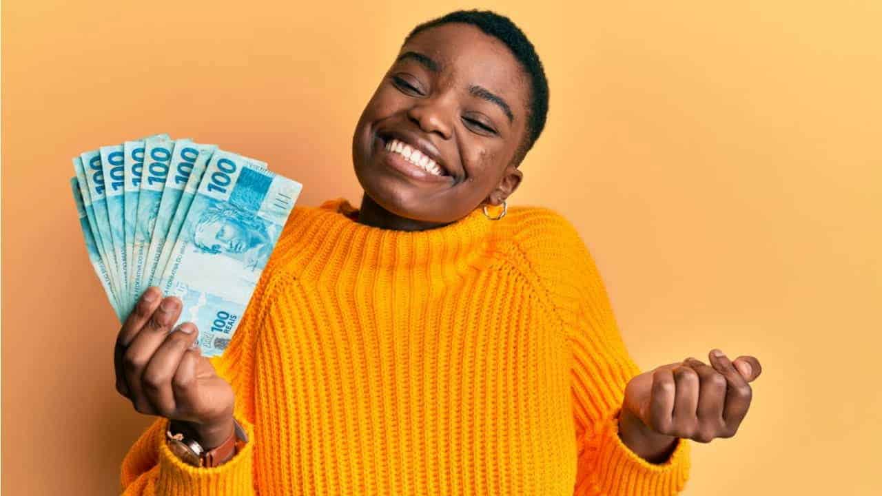 Mulher sorrindo enquanto segura notas de 100 reais