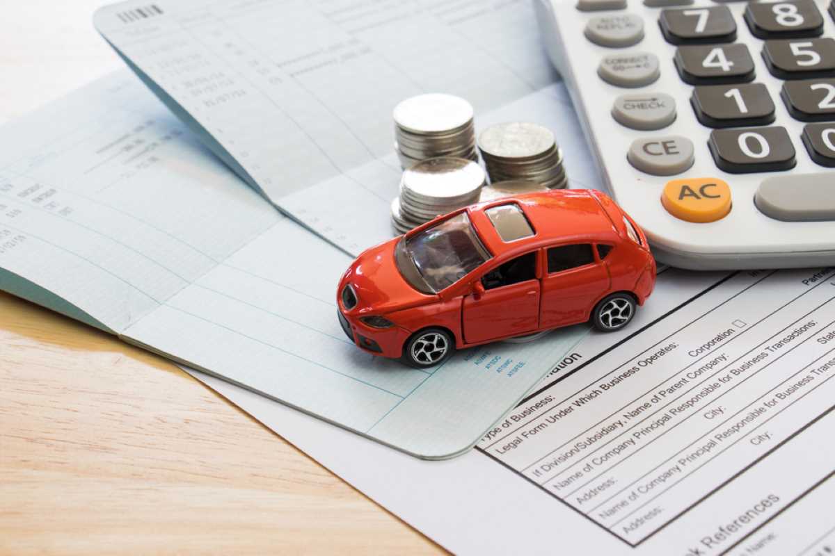 Carro em miniatura sobre papéis, moedas e uma calculadora