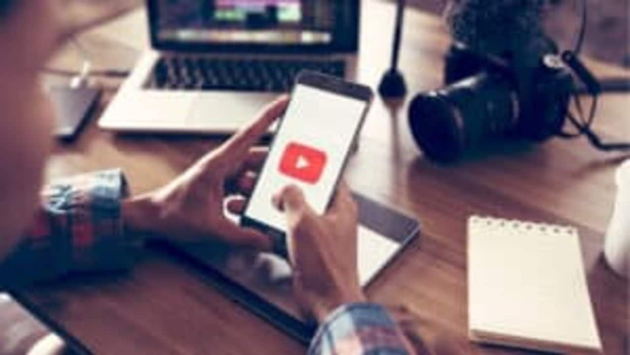 Imagem de uma pessoa acessando o YouTube pelo celular, enquanto está sentado em uma mesa.