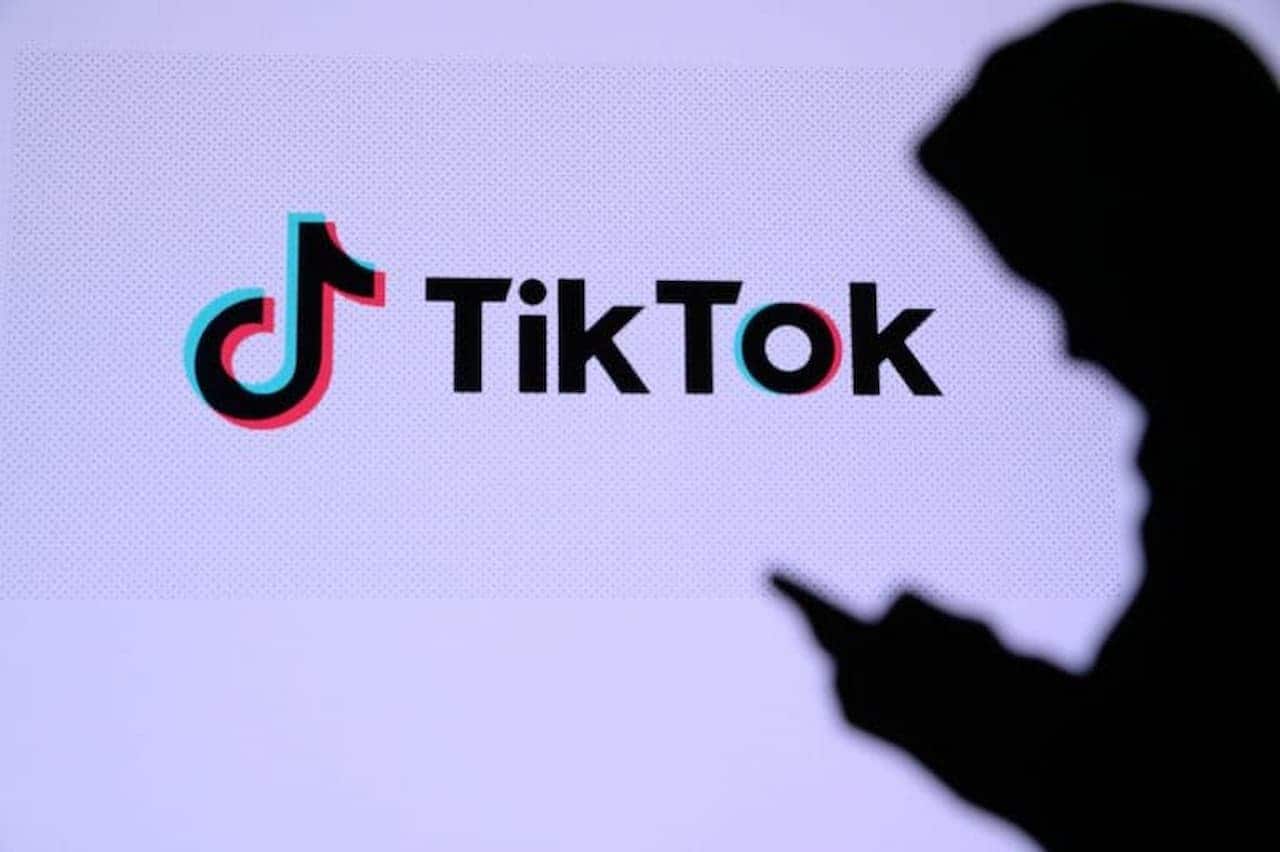 silhueta de pessoa usando o celular e nome do tiktok em uma tela ao fundo