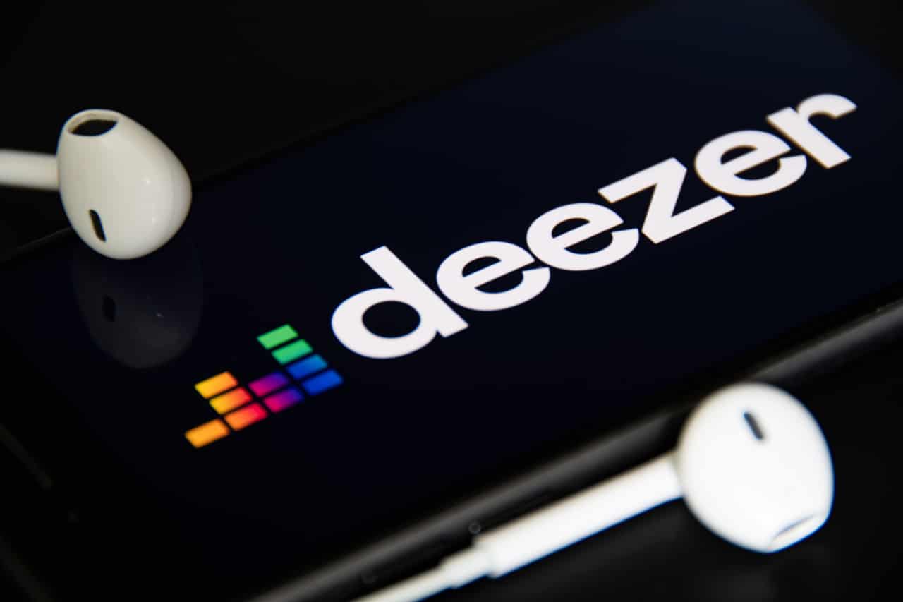 Imagem aproximada de tela de celular mostrando logo da plataforma de streaming Deezer. Ao lado, fones de ouvido.