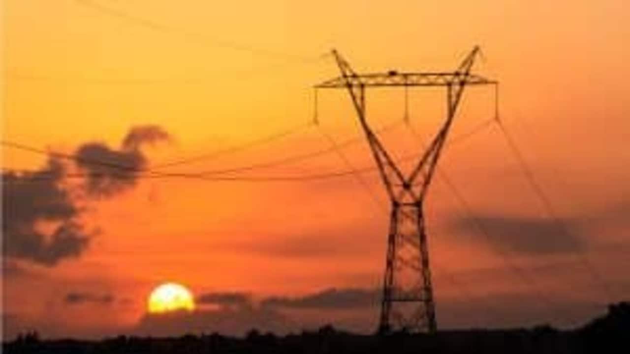 Paisagem de pôr do sol com torre de energia em destaque. A foto é bem alaranjada