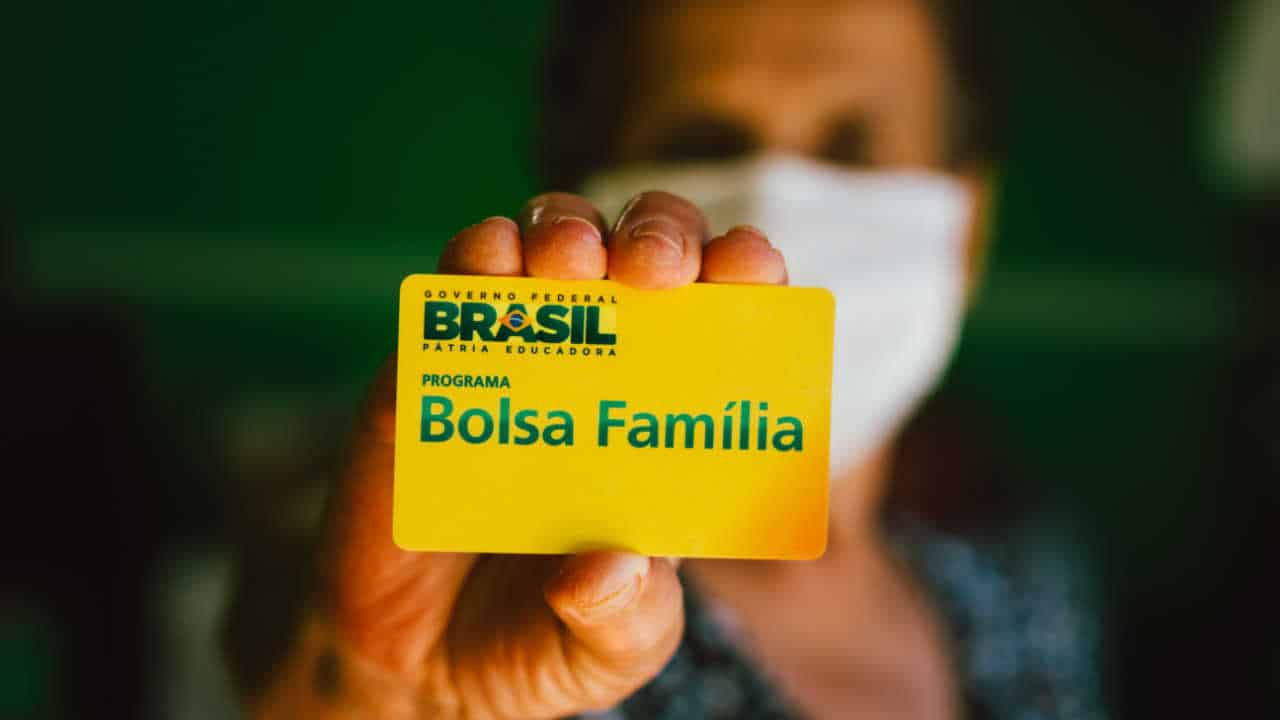Imagem de mulher segurando um cartão do Bolsa Família usando uma máscara facial branca