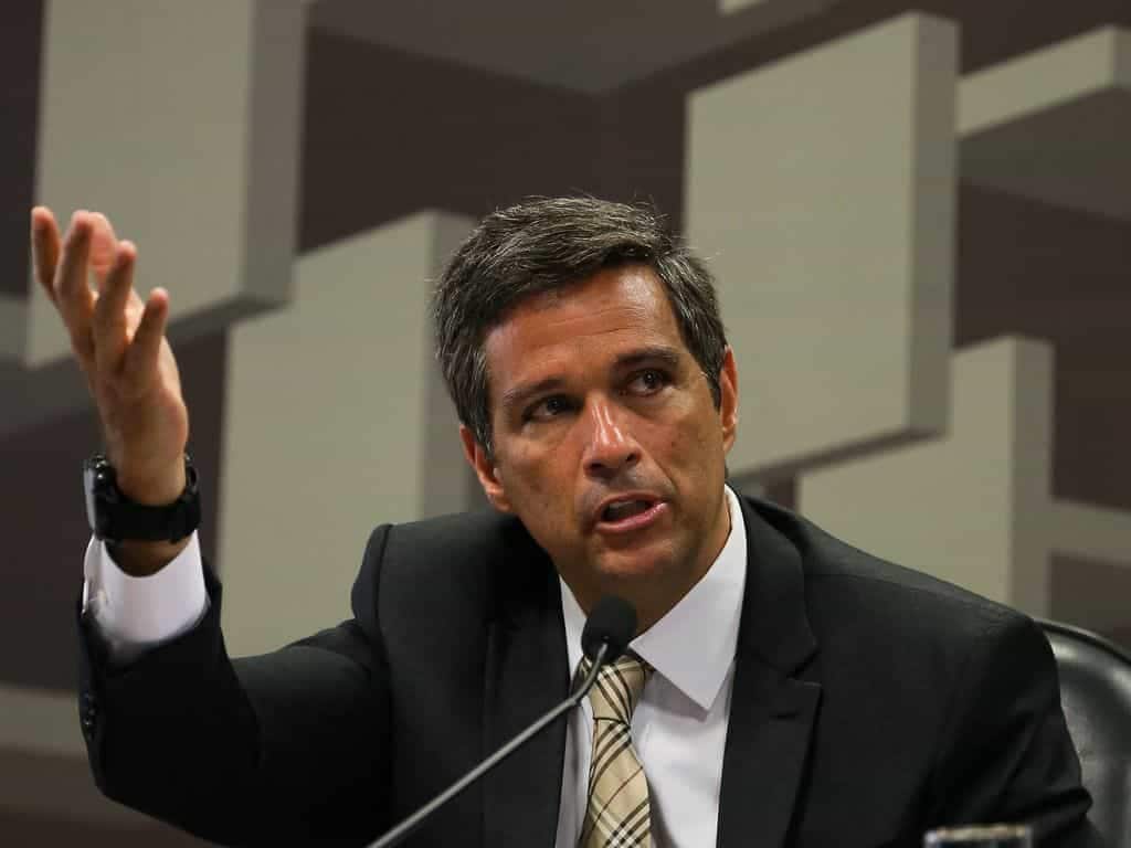 Presidente do Banco Central, Roberto Campos Neto, aparece discursando em microfone com o braço direito levantado