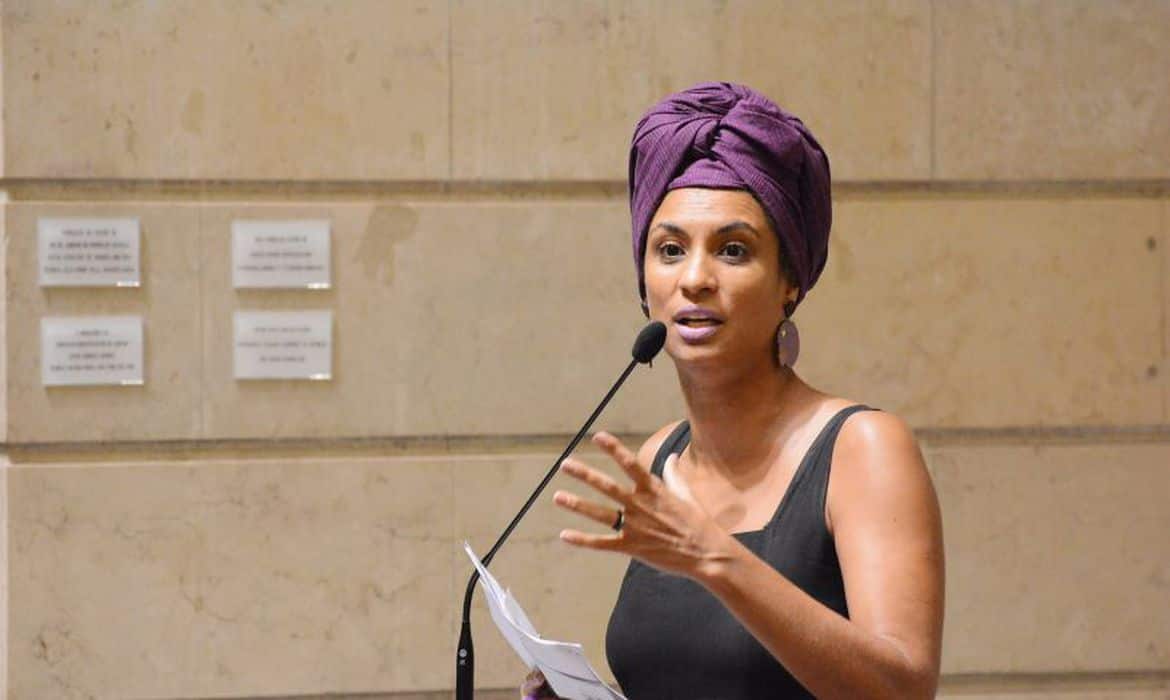 Marielle com camiseta regata preta e turbante roxo falando ao microfone em um púlpito