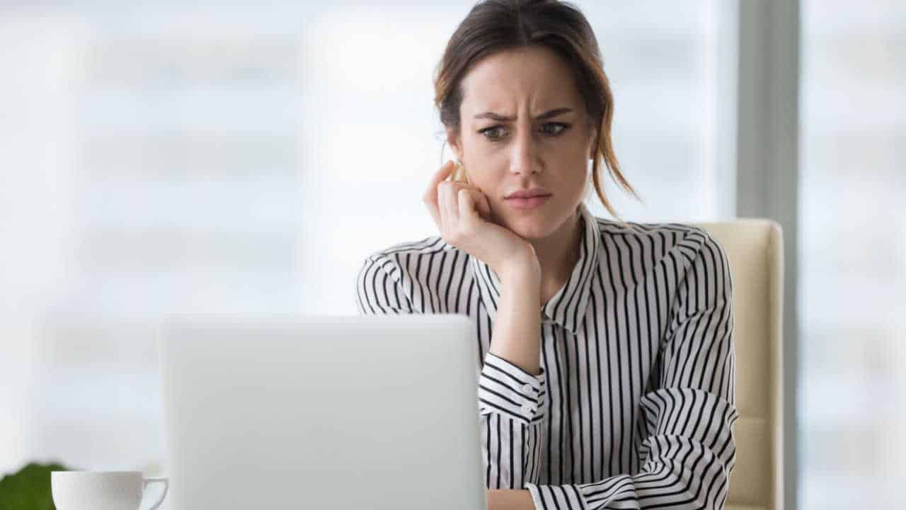 Mulher com expressão de desconfiança ao visualizar a tela do notebook, dando a entender que recebeu uma proposta de emprego falsa