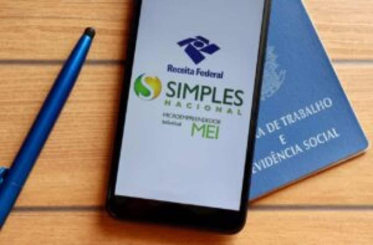 Celular com print do app Simples Nacional e carteira de trabalho em cima de mesa