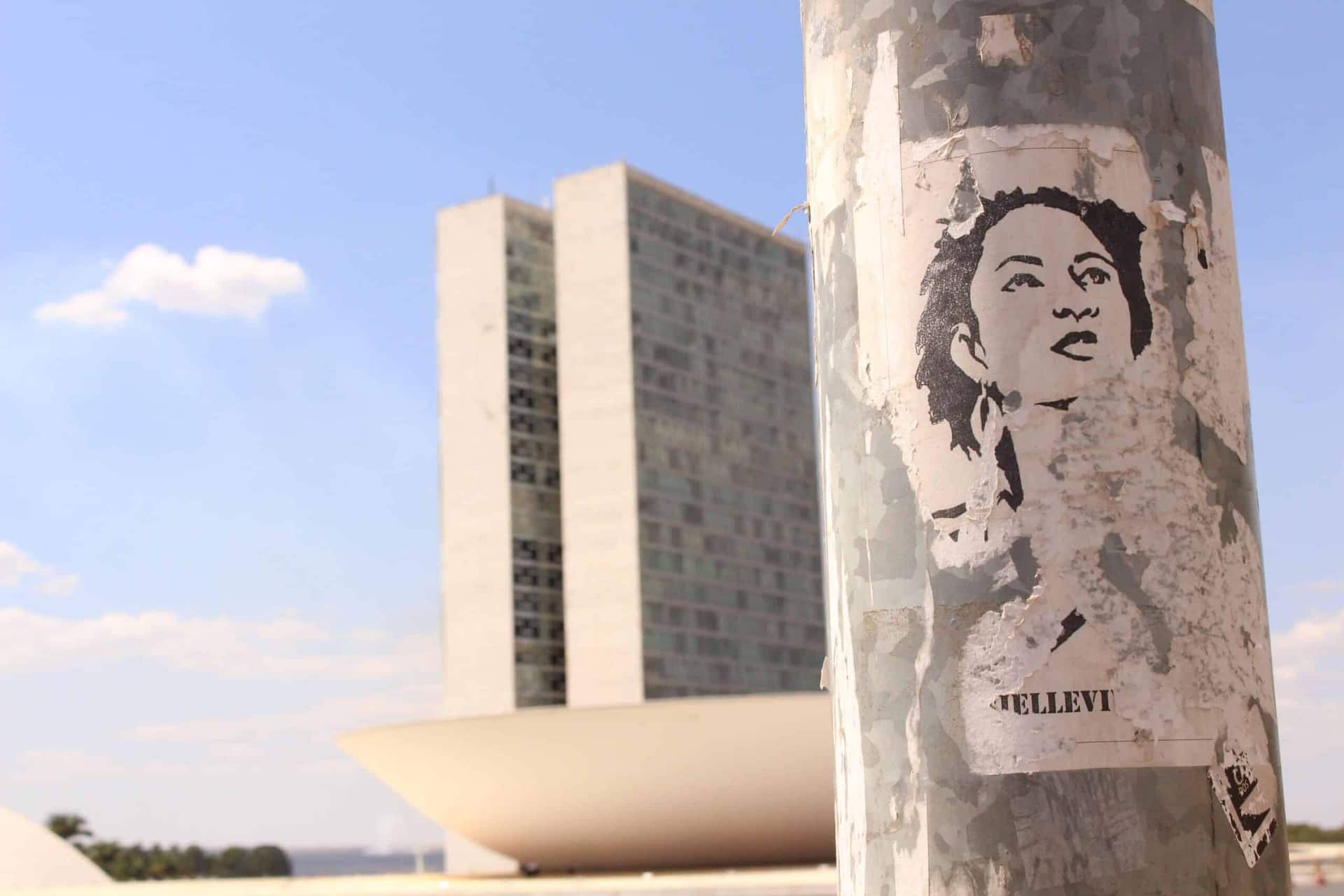Pôster com gravura de Marielle Franco colado em poste com o prédio do Congresso Nacional de fundo