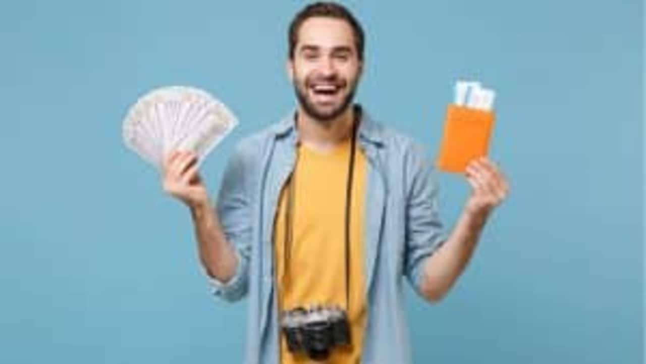 Homem sorrindo segurano cédulas de dinheiro em uma mão e passagens aéreas em outra