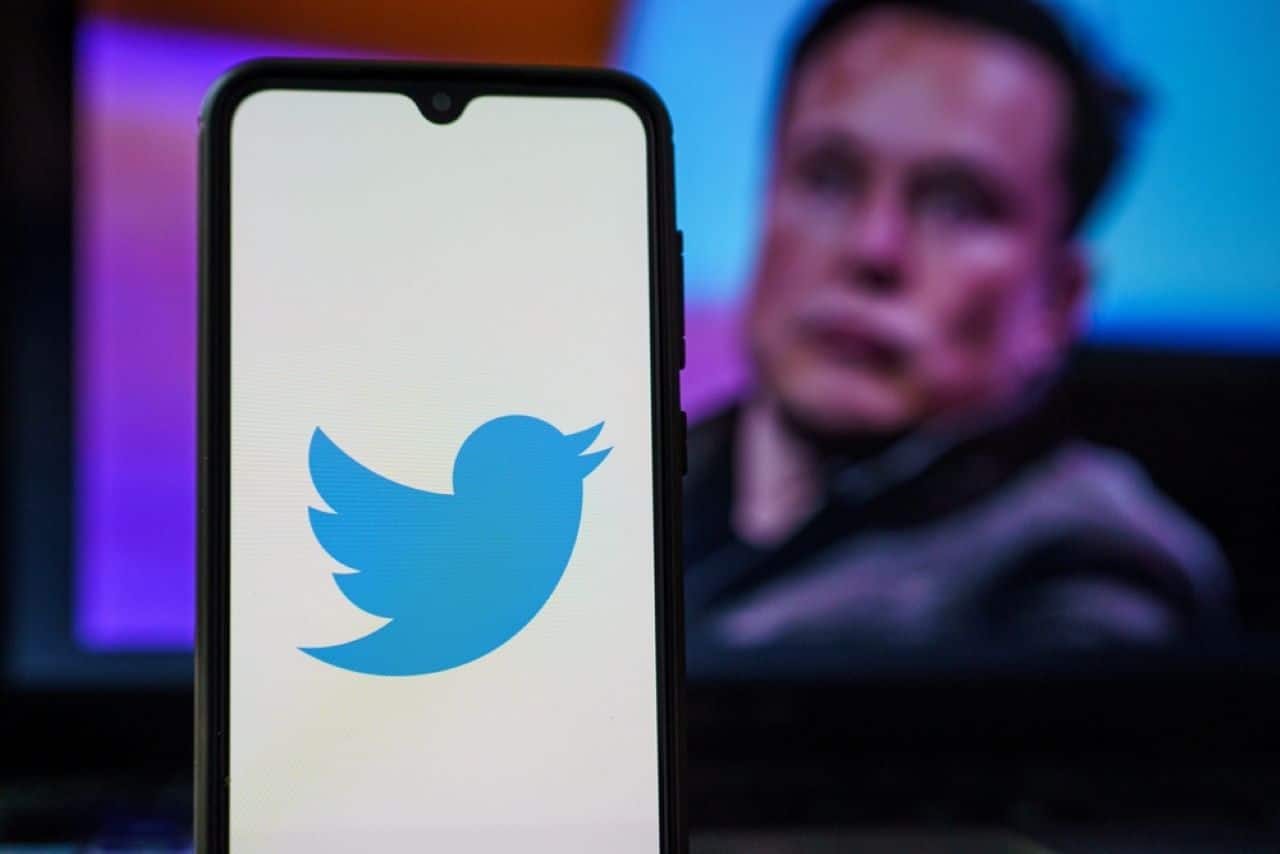 Celular com logo do Twitter na tela e Elon Musk ao fundo
