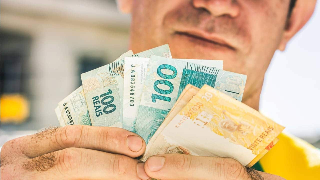 Homem segurando notas de 20 e 100 reais
