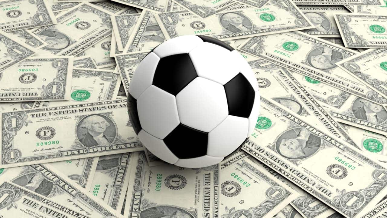 Bola de futebol posicionada sobre várias notas de dólar espalhadas