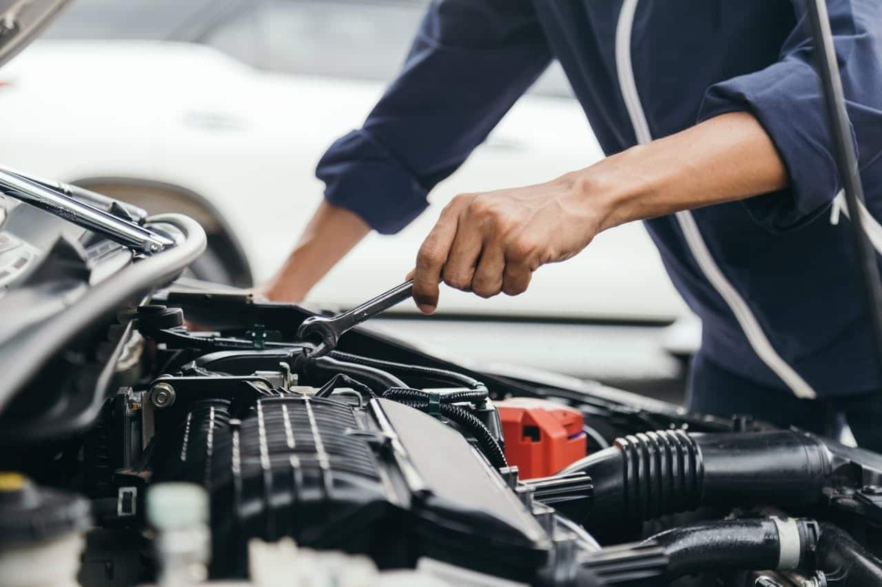 Mão segurando uma ferramenta encostada no motor de um carro