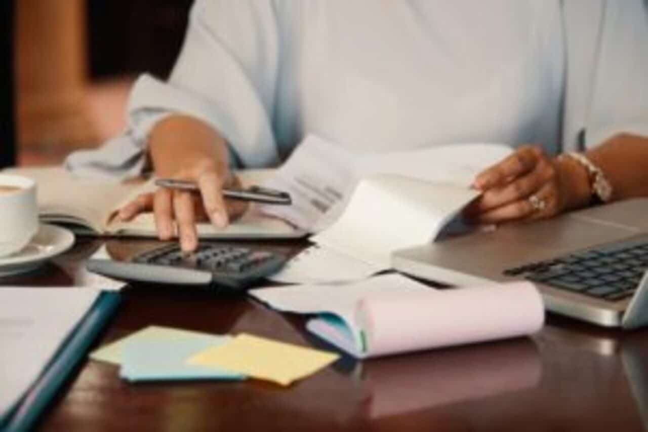 Duas mãos sobre uma mesa cheia de papéis e uma calculadora