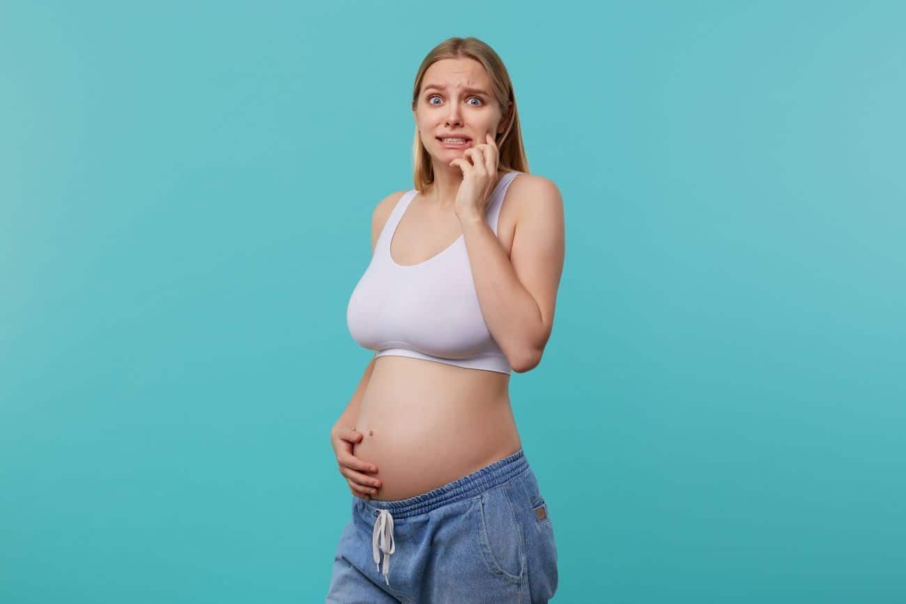 Mulher grávida com a mão na barriga e expressão de dúvida devido ao saláro-maternidade