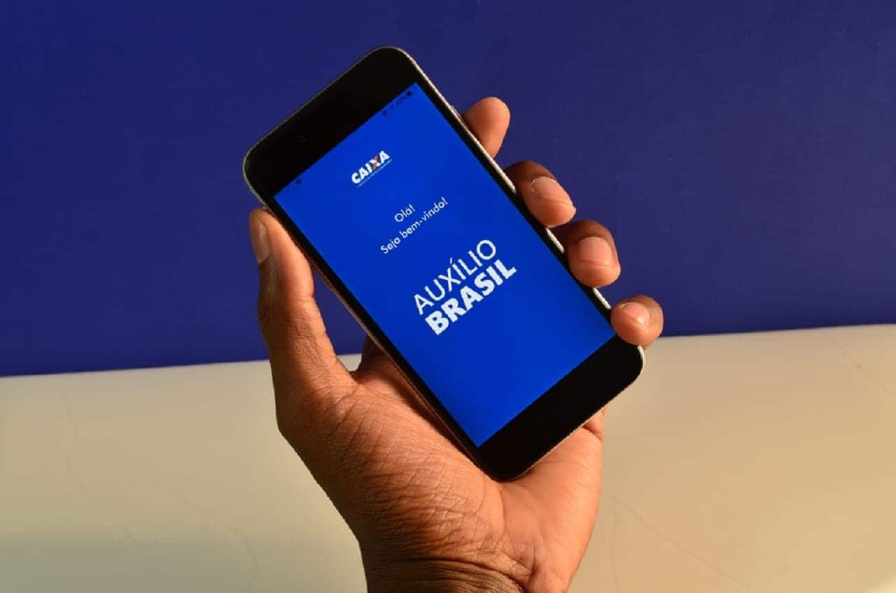 Imagem de uma pessoa utilizando o celular com a tela no logo do app do Auxílio Brasil
