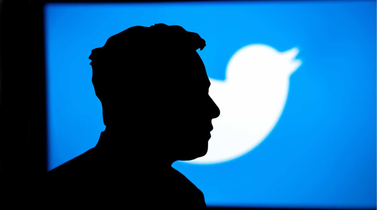 Silhueta de Elon Musk em frente a um painel com a logo da rede social Twitter.