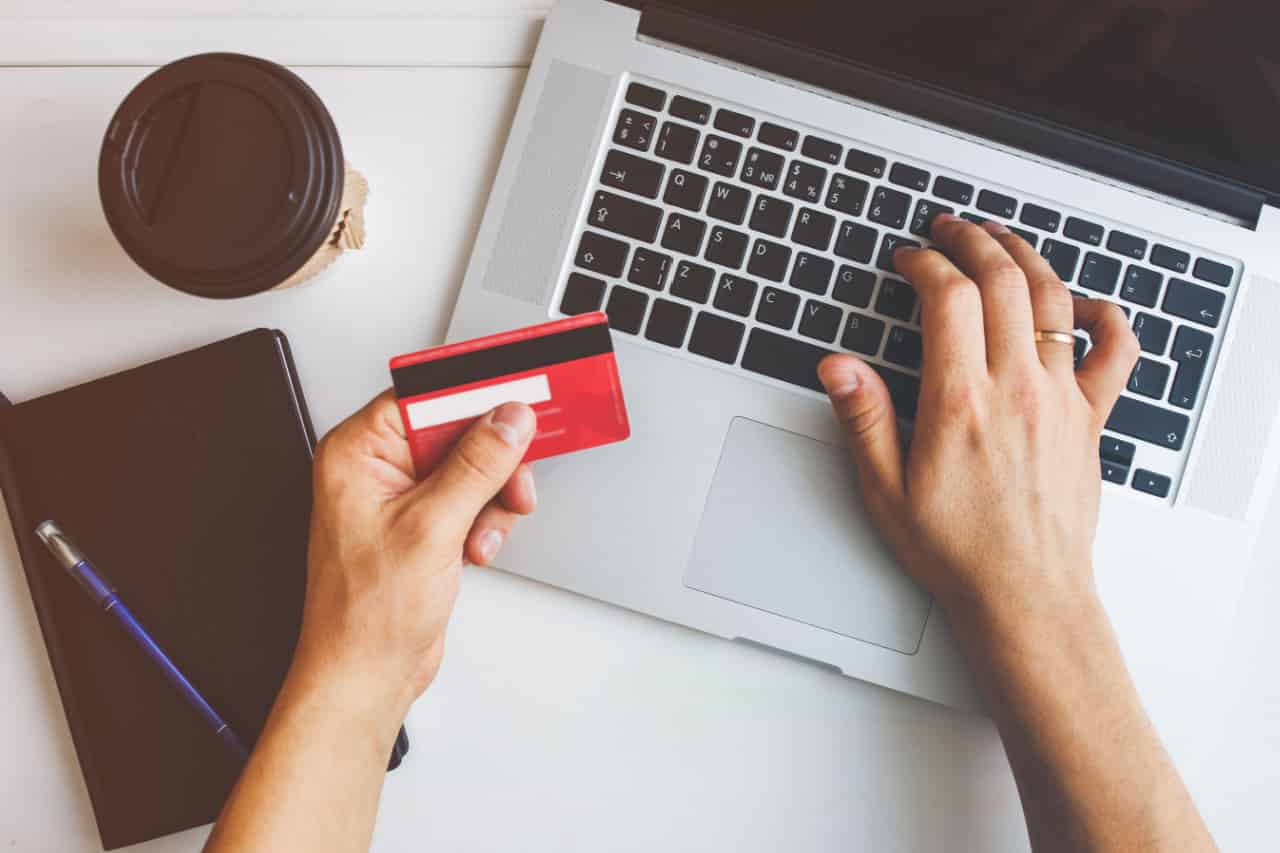 Mãos digitam número de um cartão de crédito no teclado de um notebook