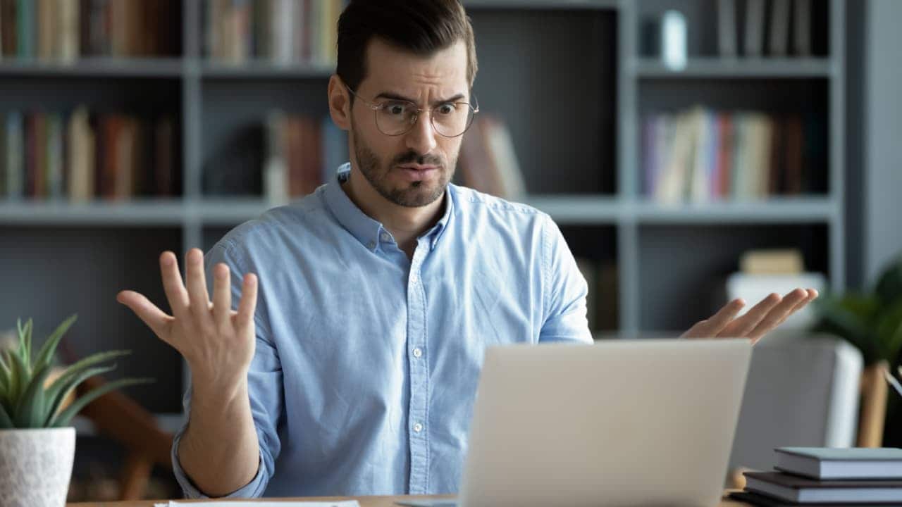 Jovem homem de óculos olha para a tela do laptop chocado