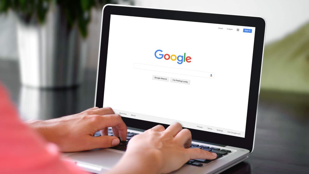 Mãos de uma pessoa utilizando um notebook cuja tela mostra página inicial do buscador do Google