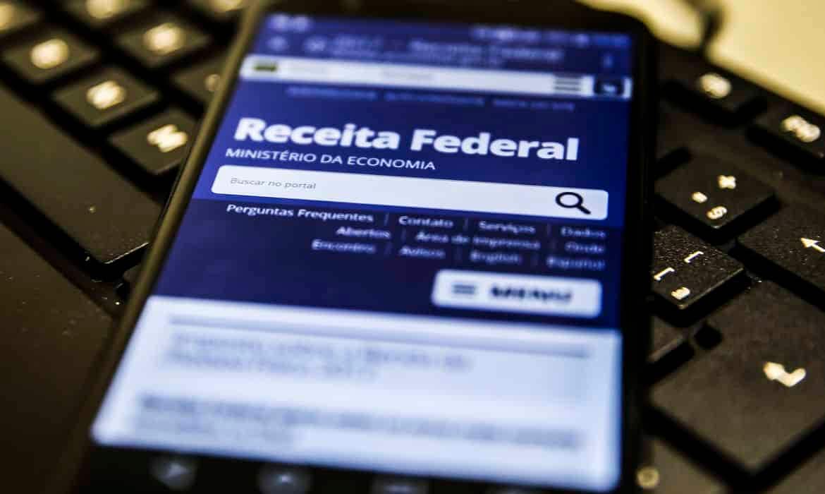 Celular apoiado em um teclado mostrando o aplicativo da Receita Federal.