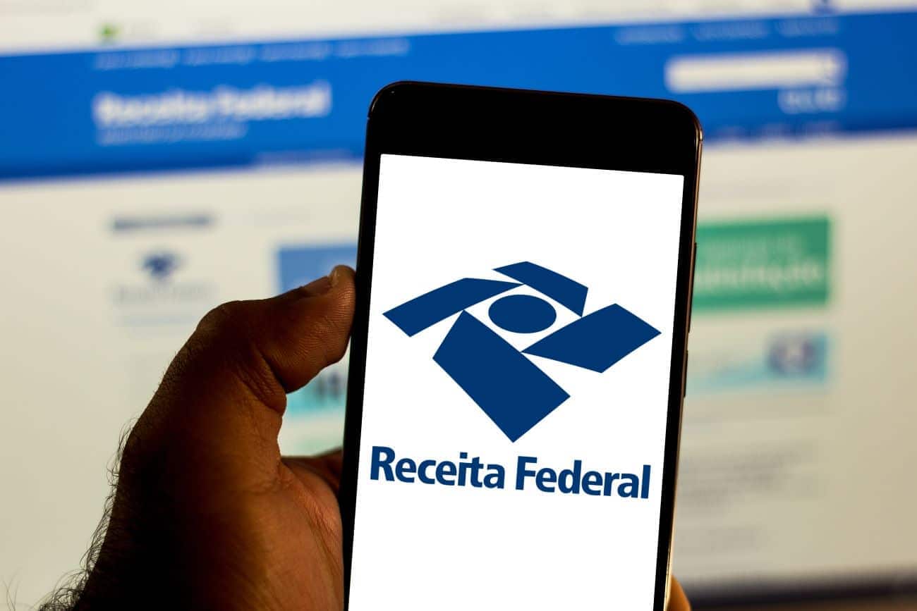 Mão segurando celular que mostra na tela a logo da Receita Federal malha fina