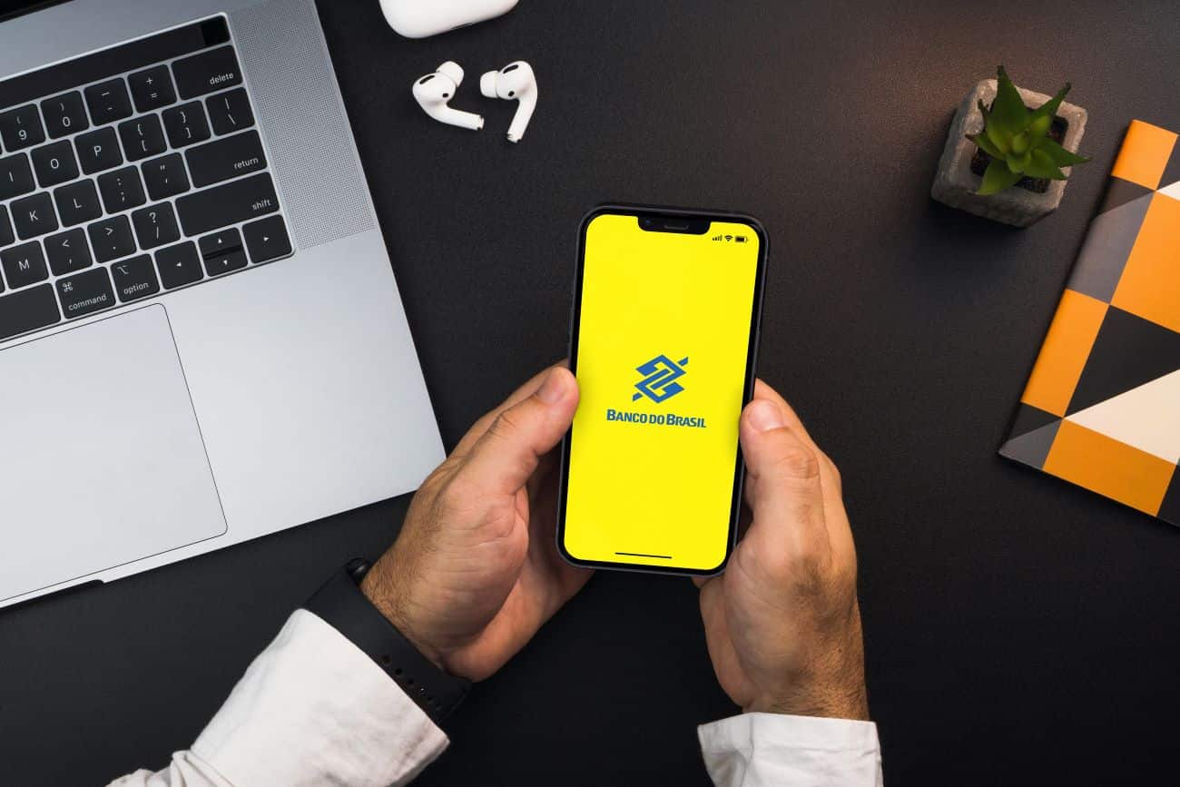 Mãos masculinas segurando celular que mostra na tela o logo do Banco do Brasil