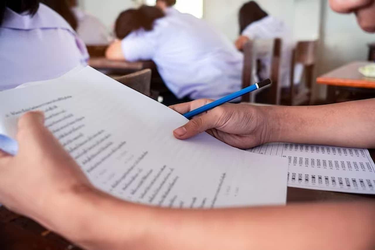 Pessoa com prova de concurso em mãos e gabarito na mesa.