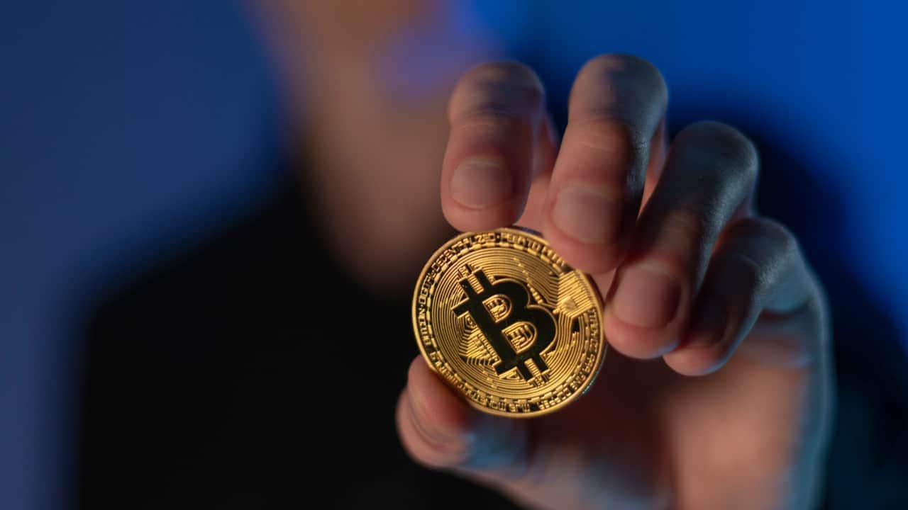 Pessoa com rosto desfocado segurando moeda Bitcoin
