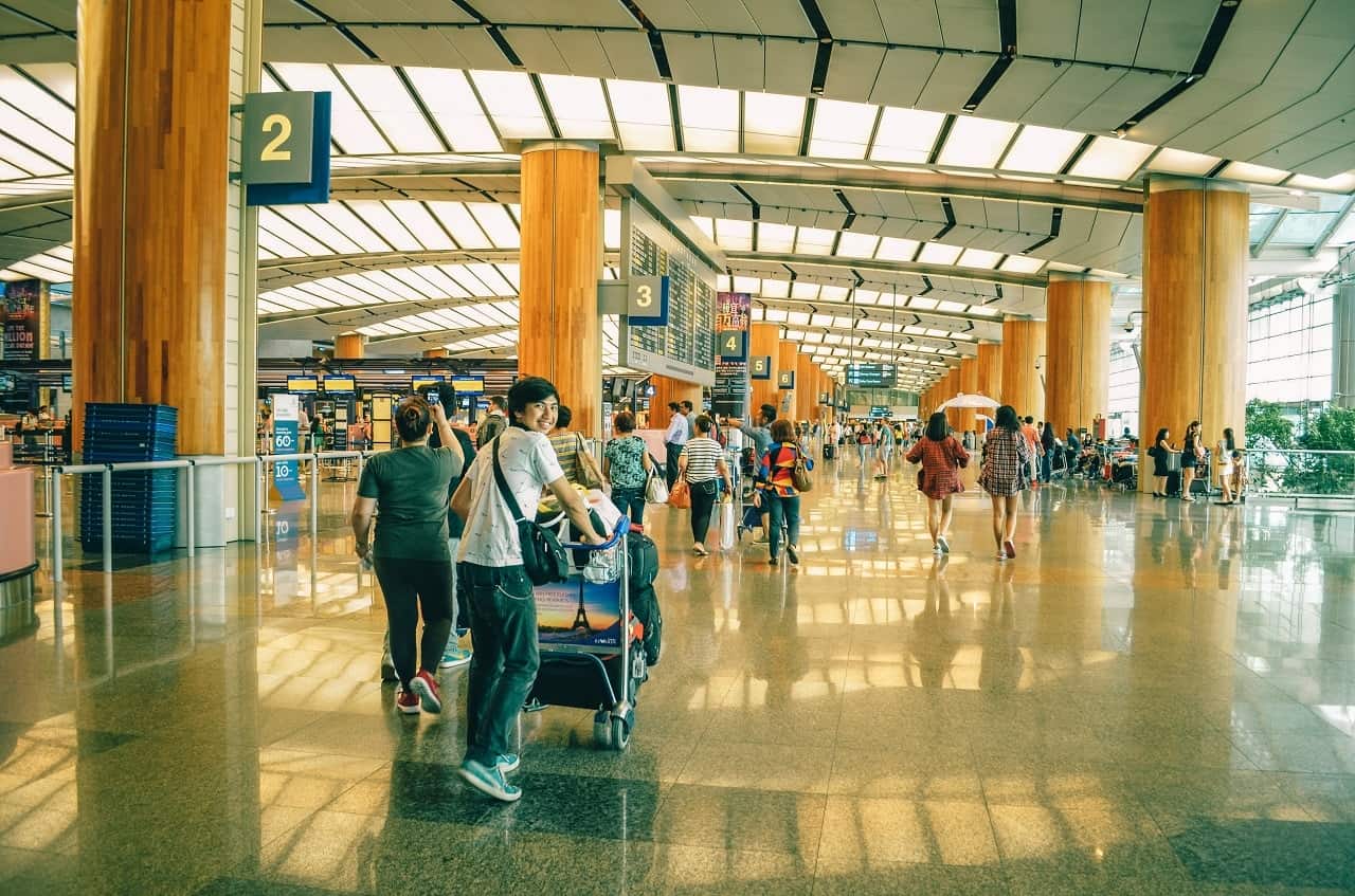 Jovem no aeroporto olha para a câmera e sorri enquanto empurra sua bagagem