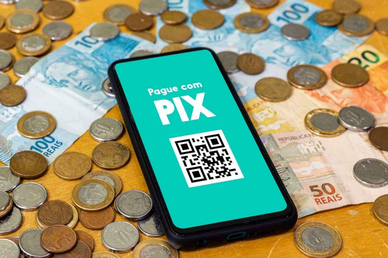 Imagem de celular com o app do Pix aberto. Embaixo, diversas notas e moedas.