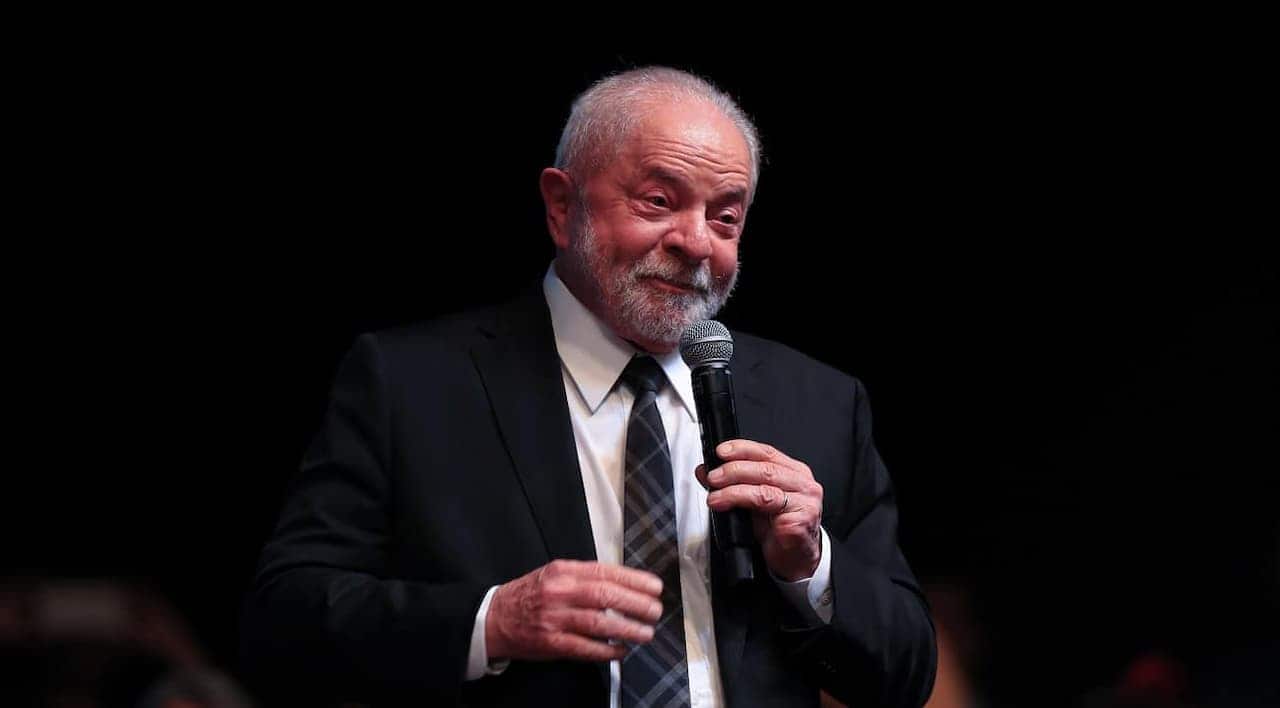 Presidente Lula vestido de terno e gravata discursando com um microfone na mão