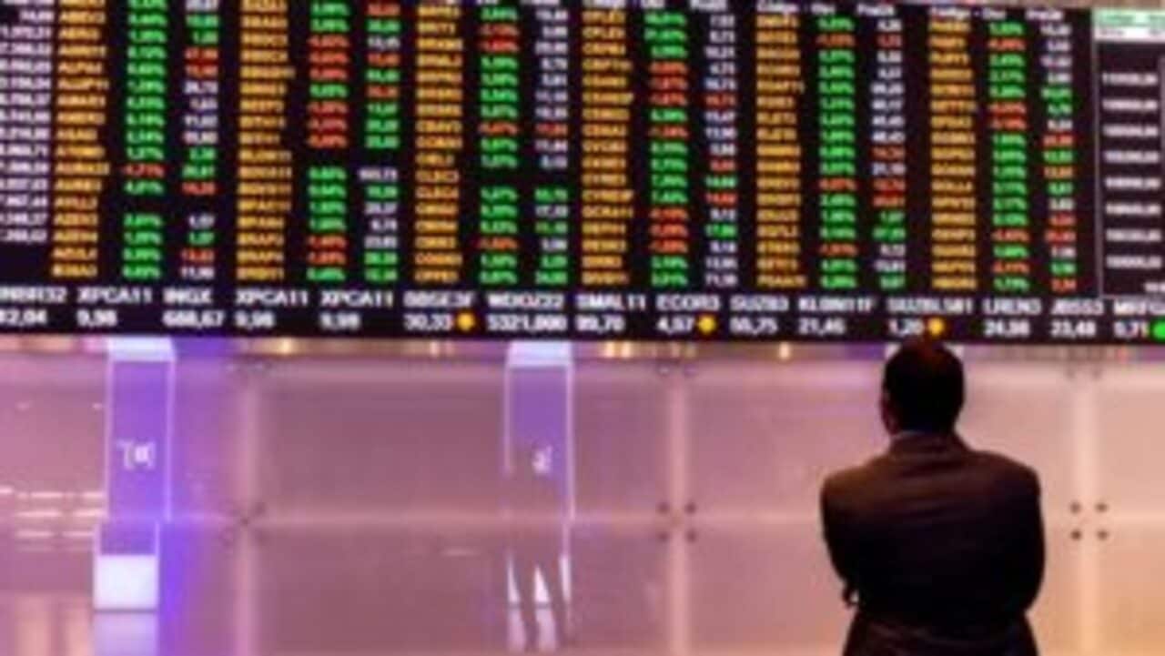 Homem de pé observando tela que mostra cotação de ações da Bolsa de Valores