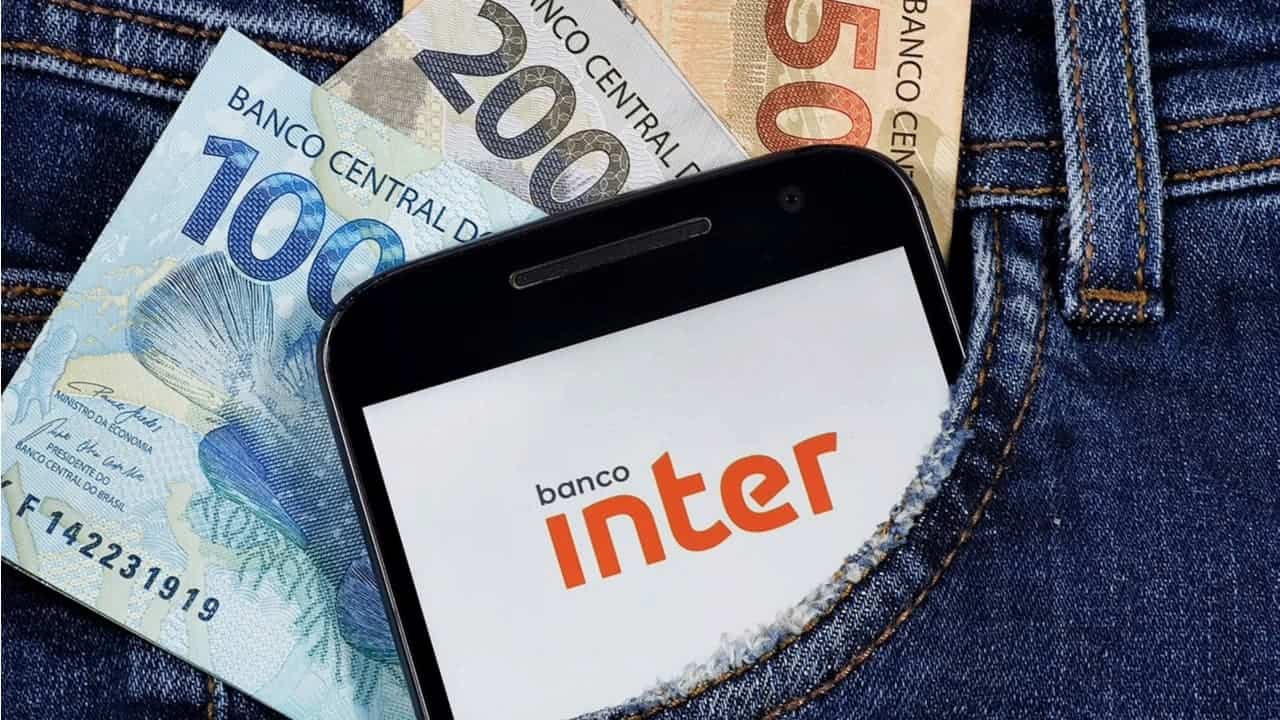 Celular com o logo do banco Inter e notas de R$ 50, R$100 e R$ 200 dentro de um bolso de calça jeans