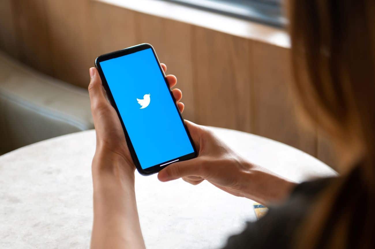 Mãos femininas segurando um celular que mostra na tela a logo da rede social Twitter