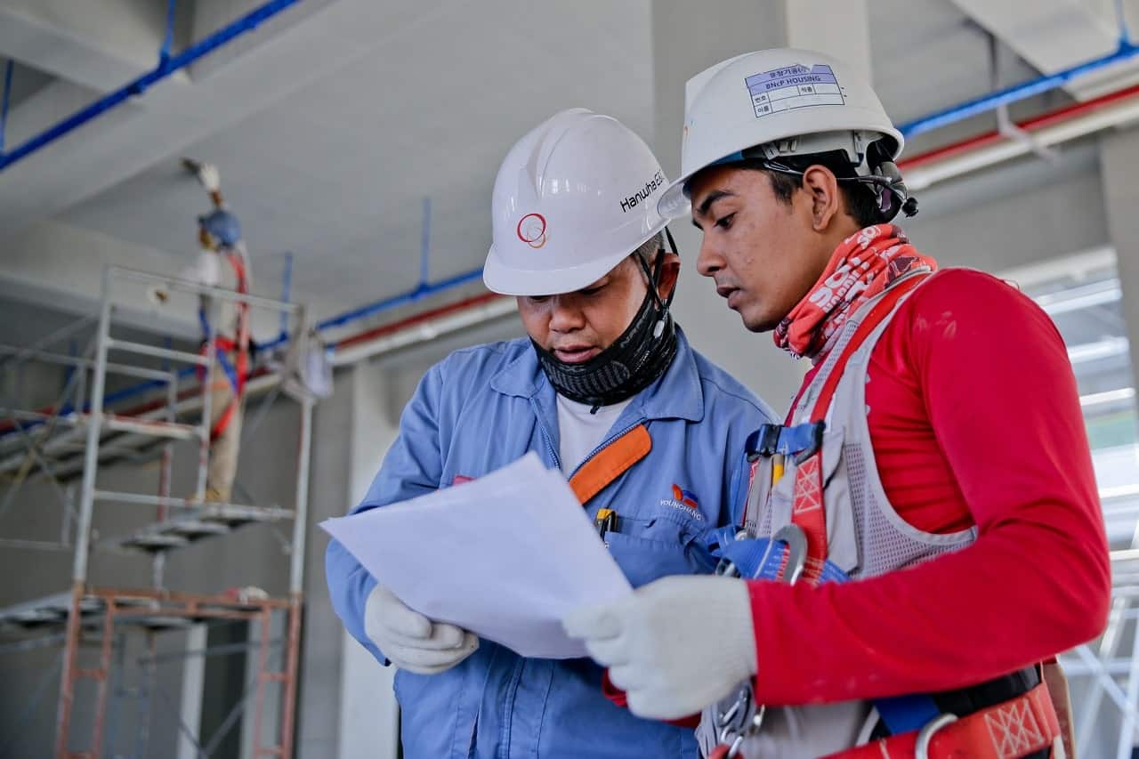 Duas pessoas com equipamentos de segurança conversando no trabalho e sobre adicional de periculosidade.
