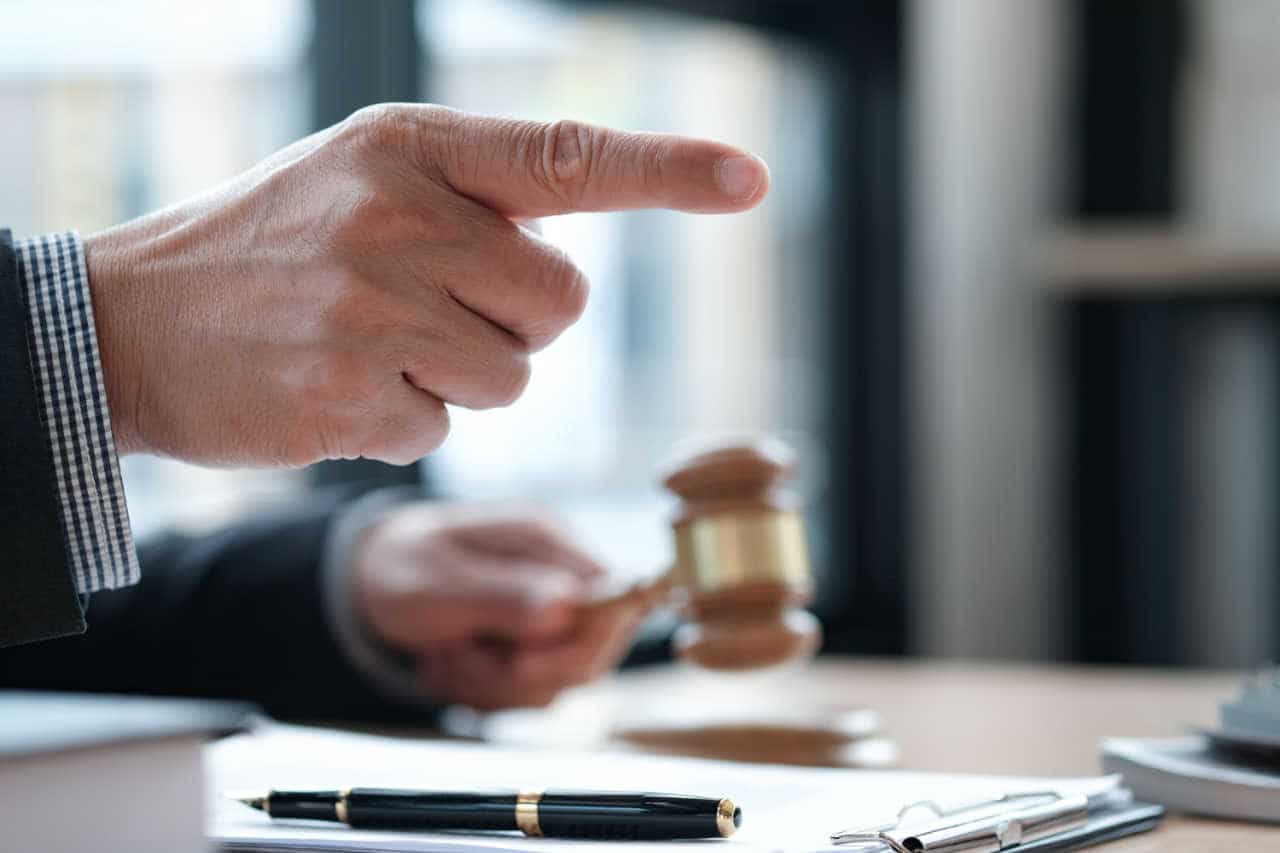 Mão segura martelo da justiça enquanto a outra aponta com o dedo em riste