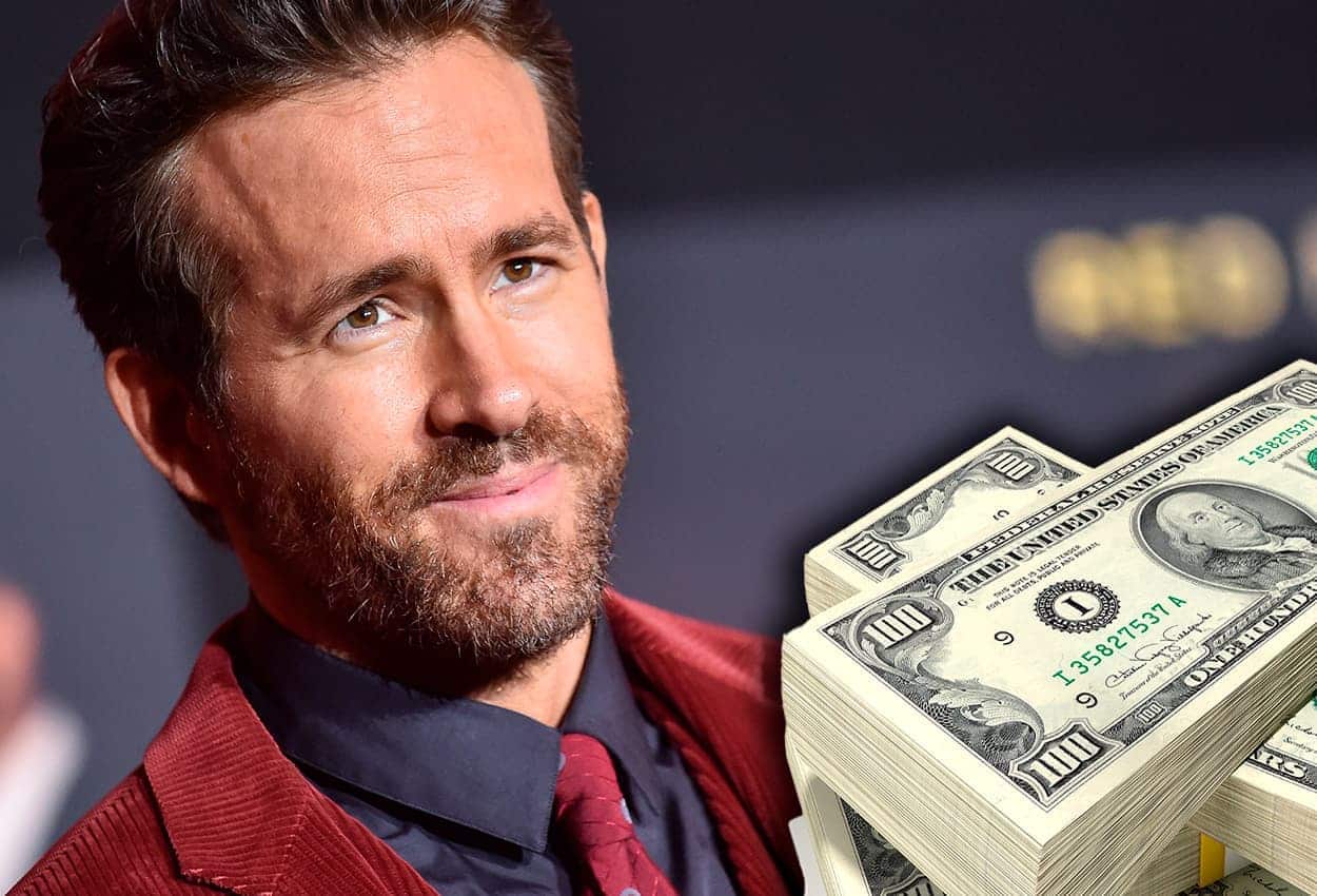 Imagem do ator de Deadpool, Ryan Reynolds. À sua frente, vários bolos de dólares.