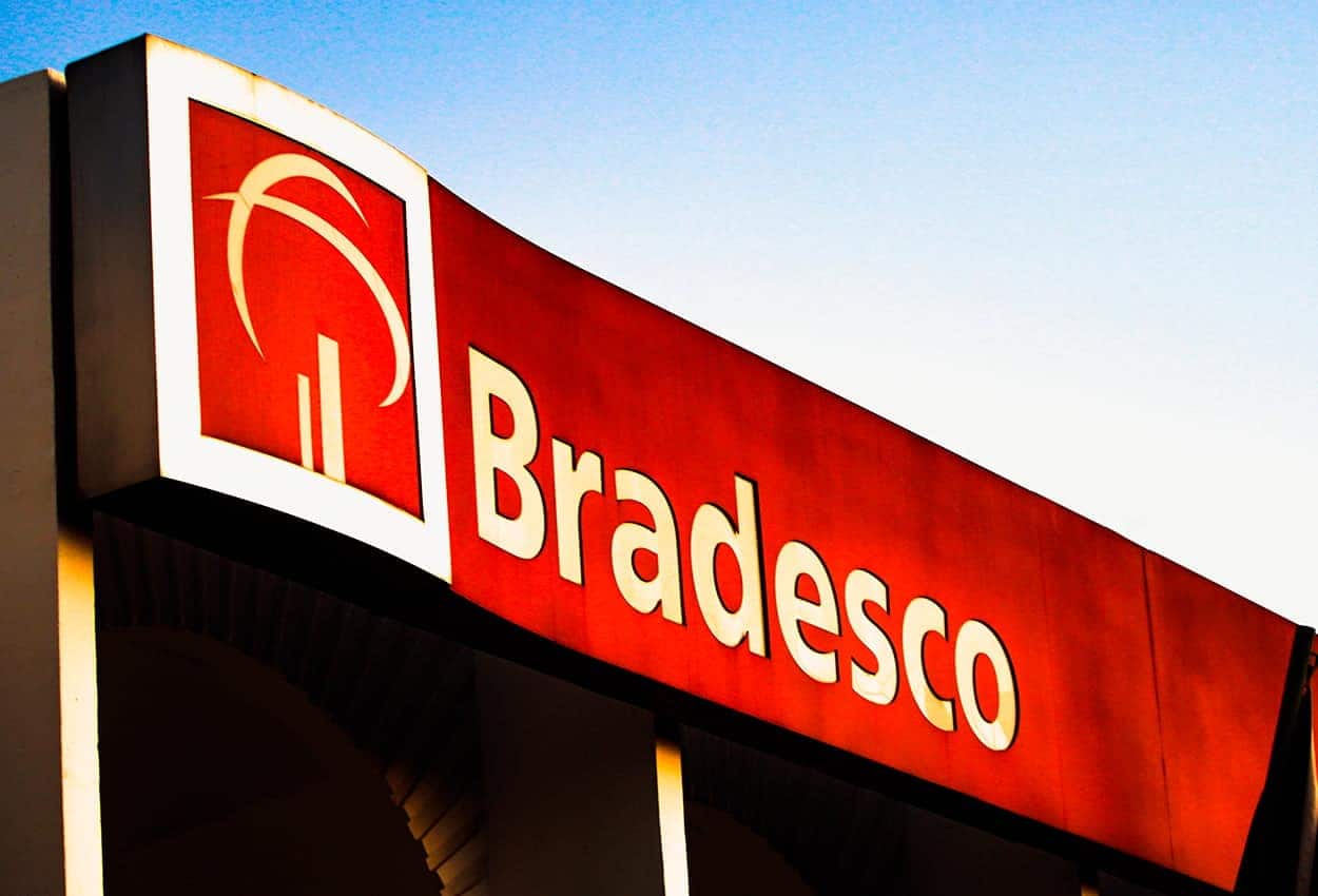 Fachada de uma agência do Banco Bradesco com letras e símbolo brancos em fundo vermelho
