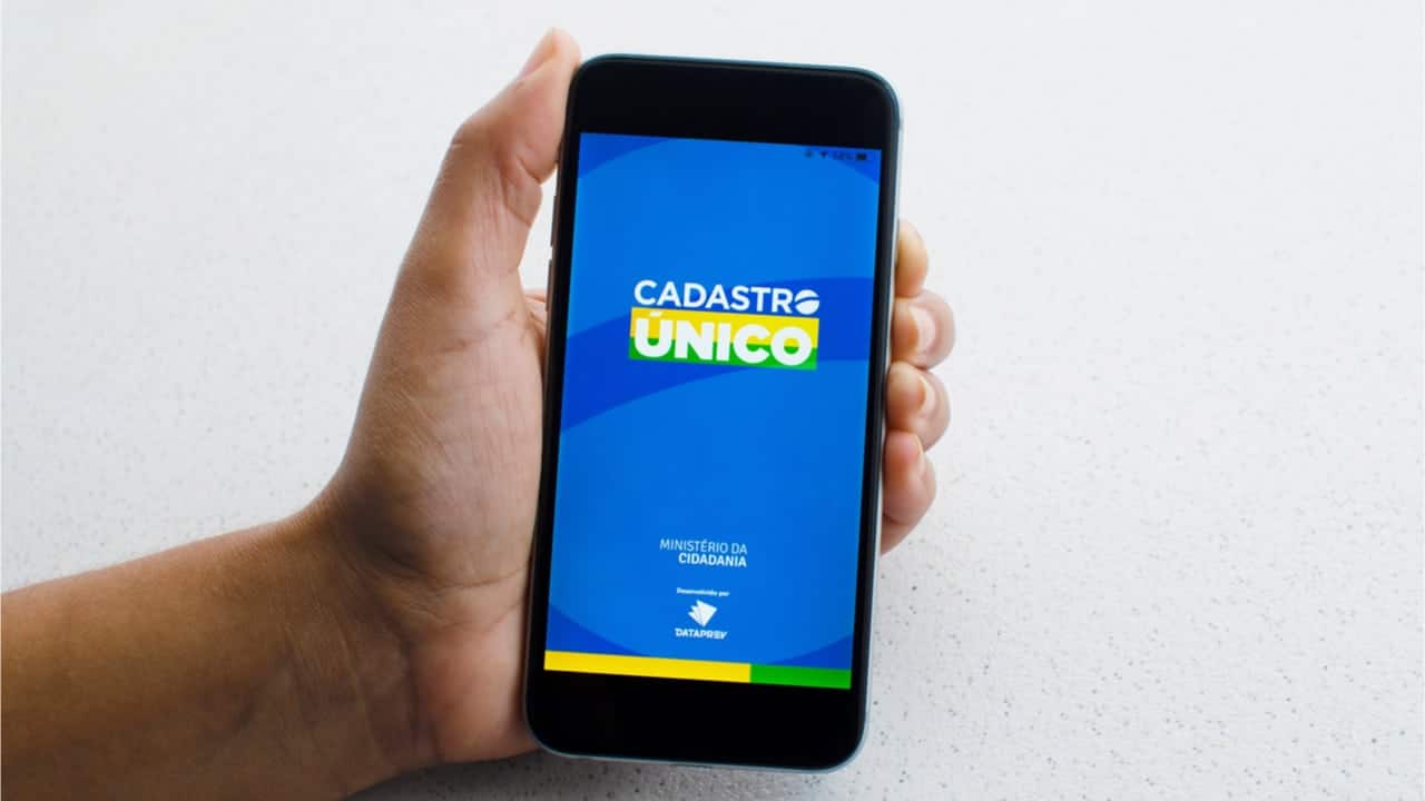 Mão segurando celular com aplicativo do CadÚnico, o Cadastro Único para Programas Sociais do Governo Federal