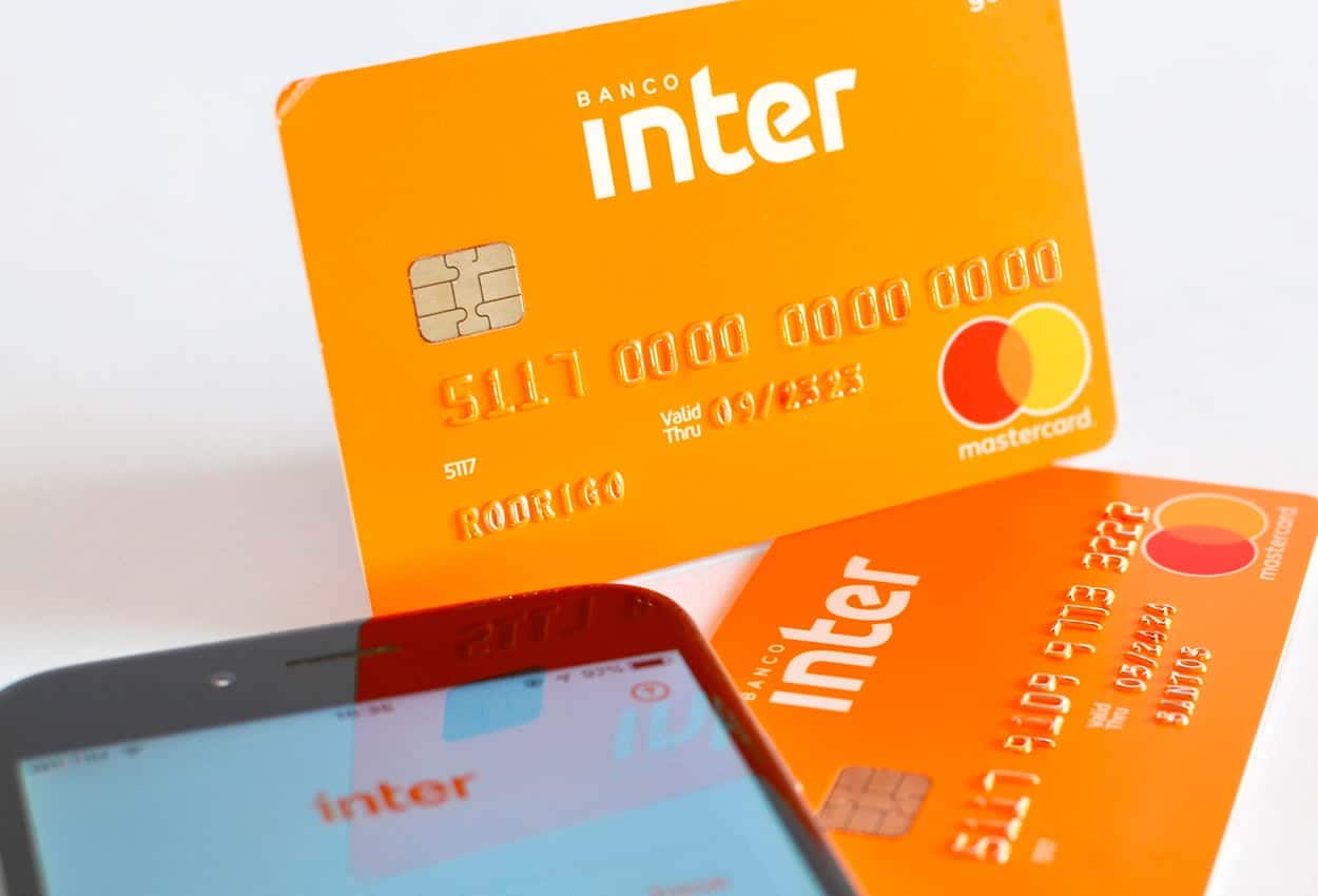 imagem de cartões de crédito ou débito do banco Inter ao lado de celular com aplicativo do Banco Inter aberto imagem com fundo branco