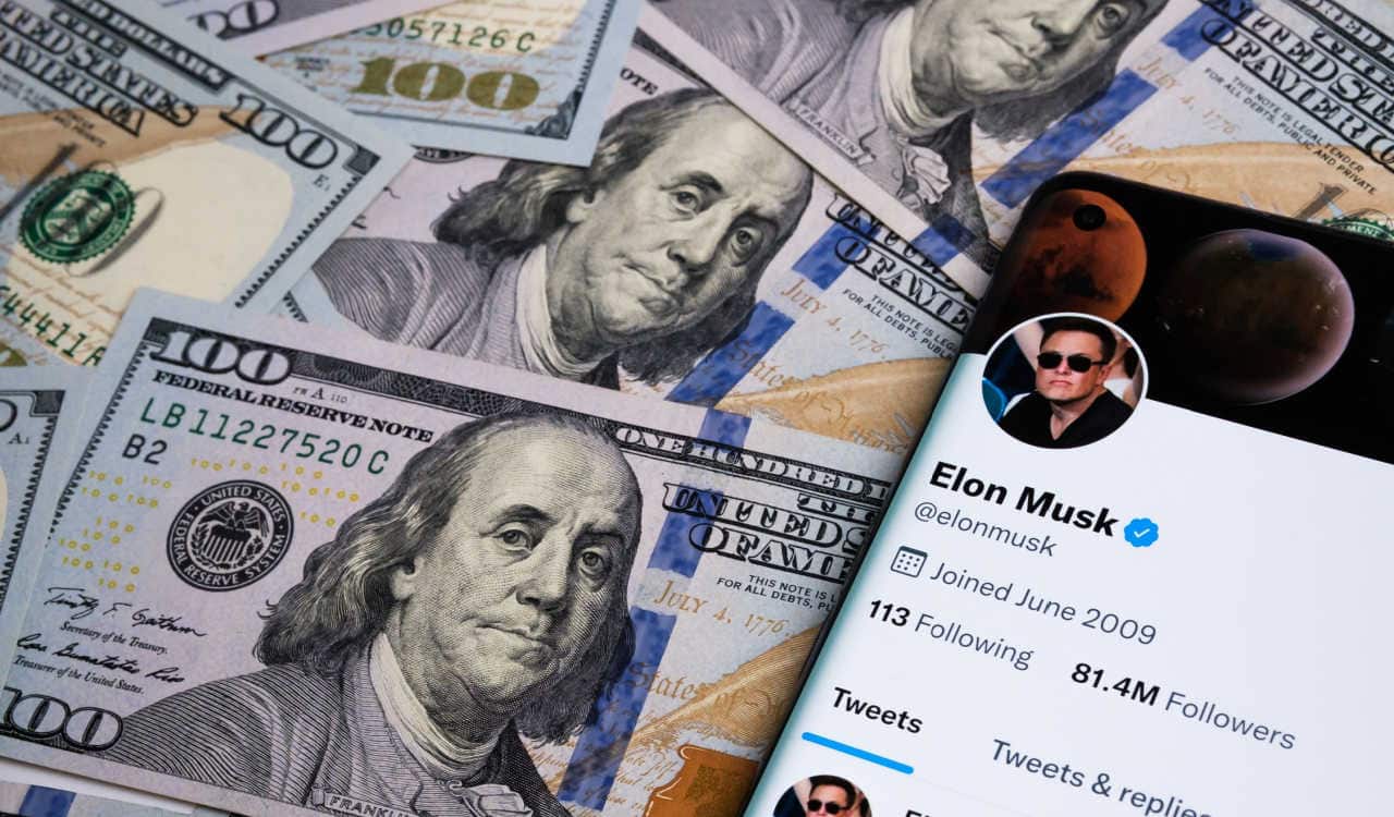 Celular por cima de várias notas de dólar. Na tela do aparelho aparece o perfil de Elon Musk no Twitter.