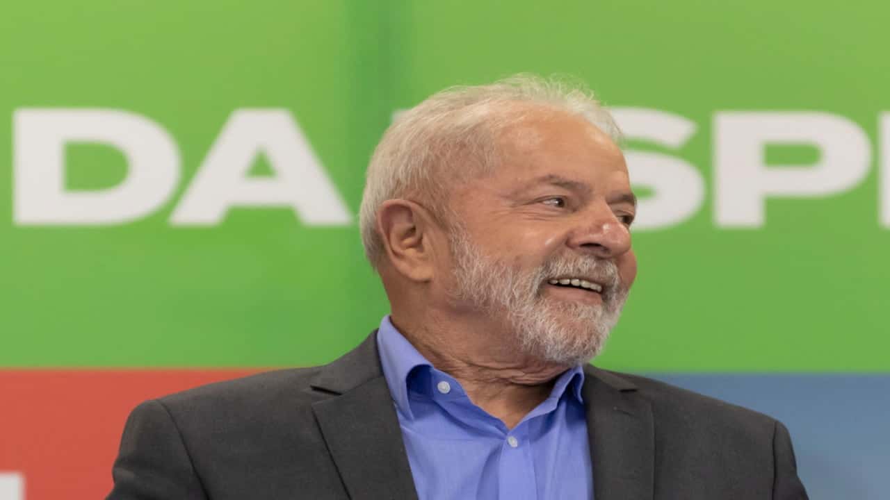Presidente Lula olhando para a esquerda com semblante alegre em frente a um fundo verde