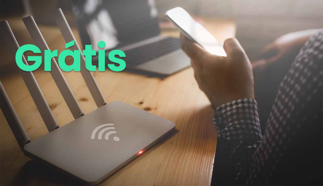 Pessoa sentada segurando um celular em frente a um notebook e do lado de um roteador wi-fi