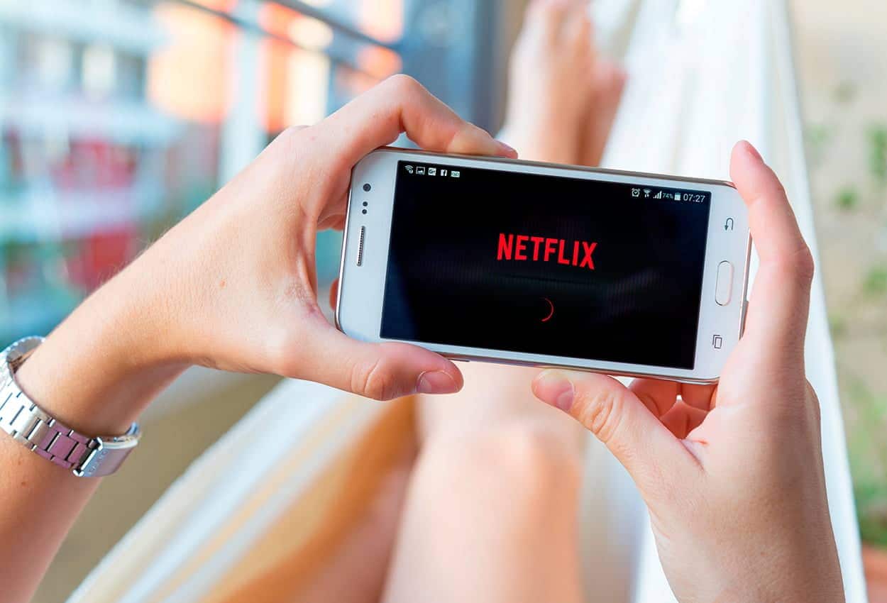 Maos segundando celular com aplicativo da Netflix