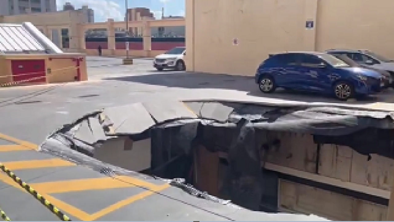 Imagem exterior de um estacionamento de shopping com uma cratera enorme no chão